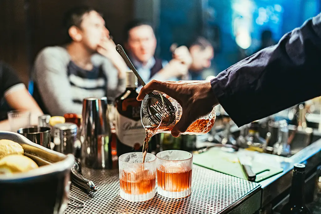 Bartender pouring a drink into two glasses.