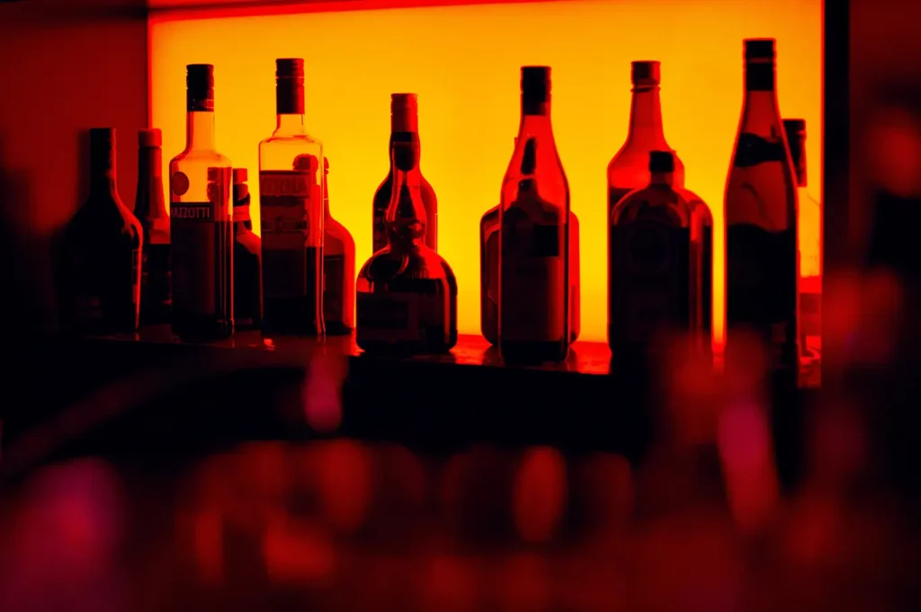 Various bottles of liquor on a shelf backlit by a yellow light.