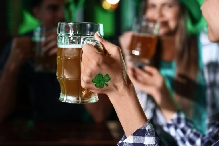 A woman's hand with a shamrock painted on it holds up a mug of beer.