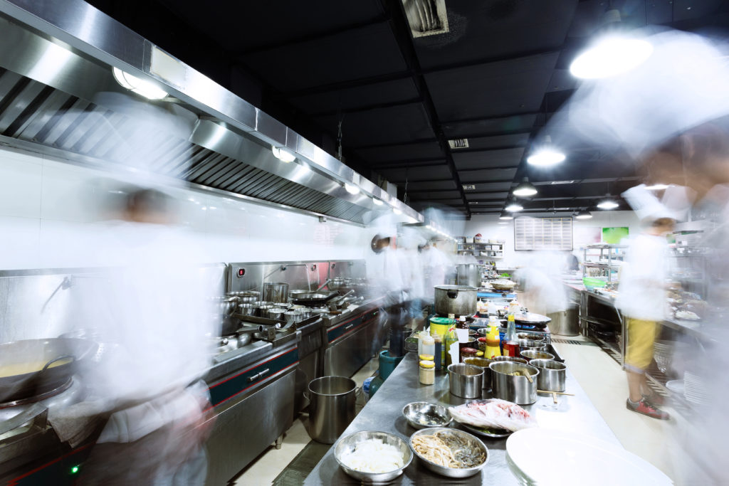 A long-exposure shot of a commercial kitchen with multiple chefs manning stations and preparing food.