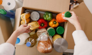 A pair of hands are reaching into a brown cardboard box on a countertop. The box is full of food product items protected by product liability insurance.