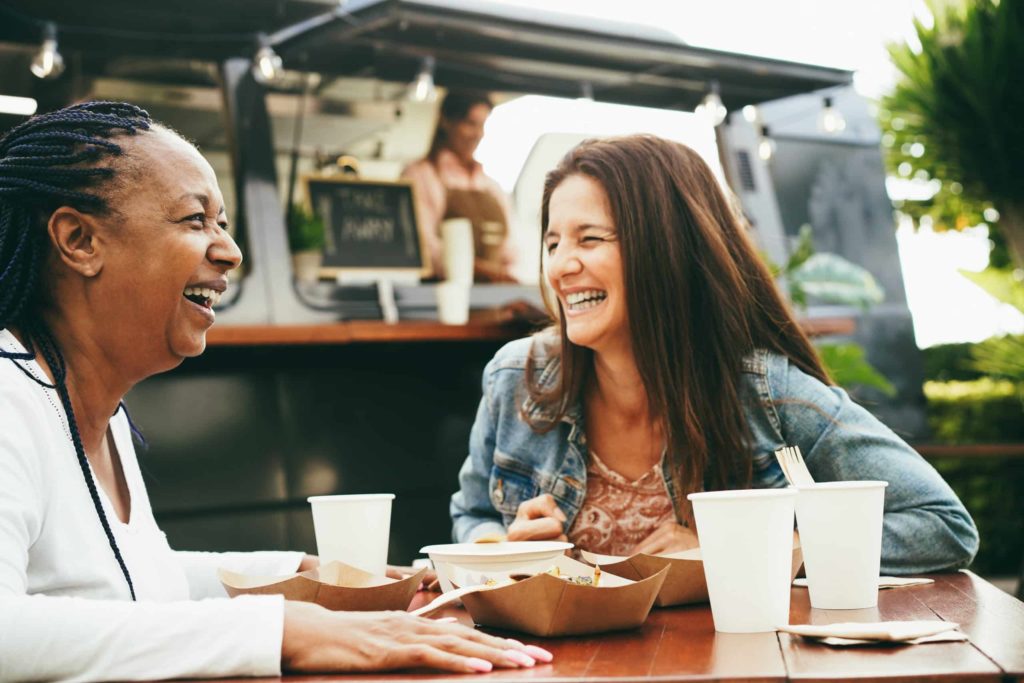 Happy multiracial senior women eating at food truck restaurant outdoo