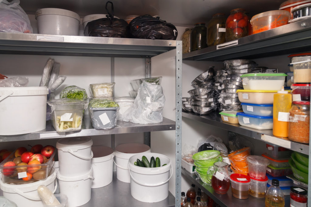 An assortment of dried foods, fruit, vegetables, and pre soaked dishes stored on shelves in a restaurant.