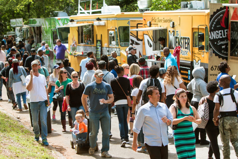 Several food trucks lined up, attracting a large crowd at a community event.