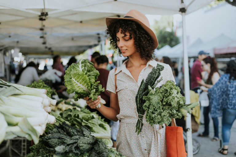 A woman in a white polka dot sundress buying produce at a farmers market stall.